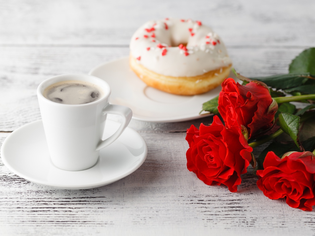 Чашка кофе, пончик и три красных розы на столе
