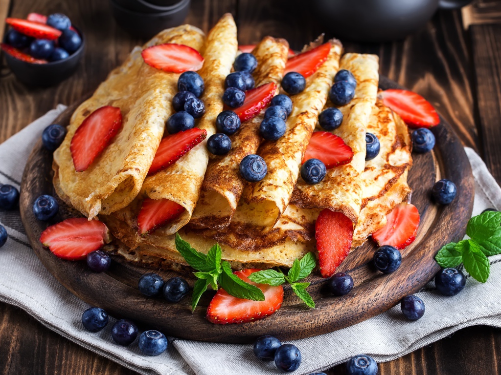 Вкусные тонкие блинчики на деревянной доске с ягодами черники и клубники 
