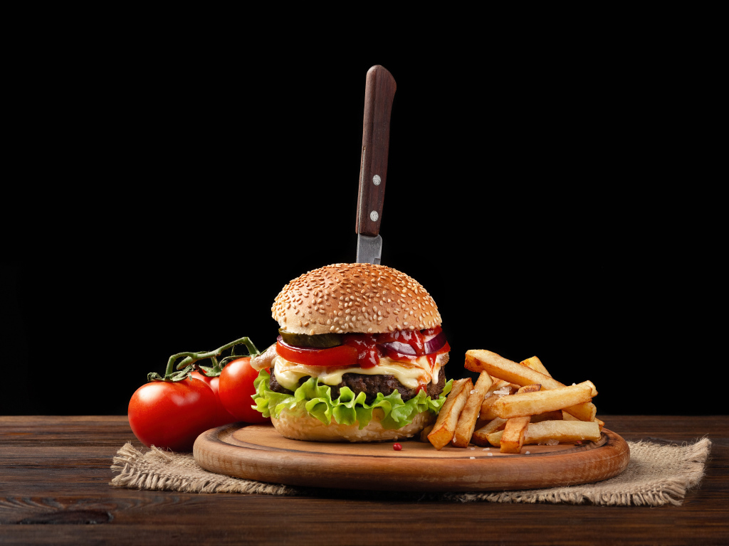 Гамбургер с ножом на столе с помидорами и картофелем фри 