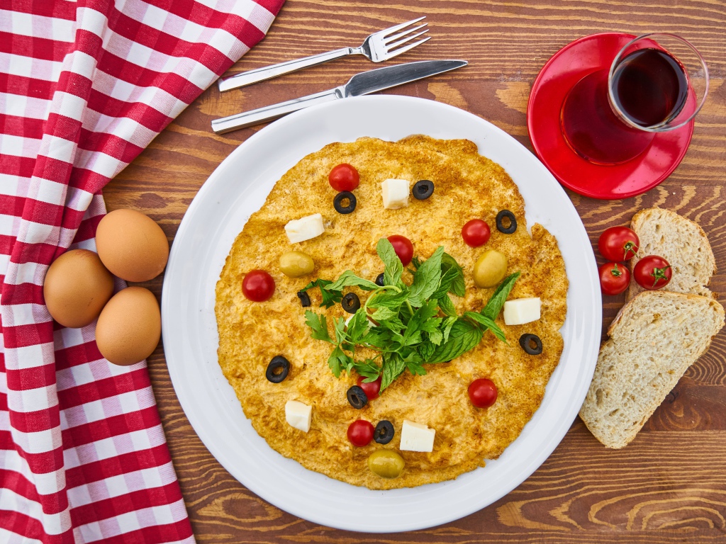 Omelet on the table with tea, tomatoes, eggs and bread