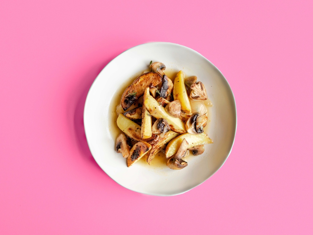 Картофель с грибами в тарелке на розовом фоне 