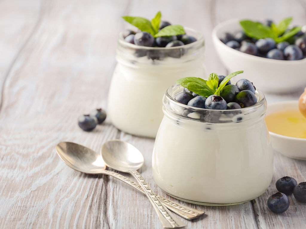 Йогурт в банках с ягодами черники на столе с ложками и медом