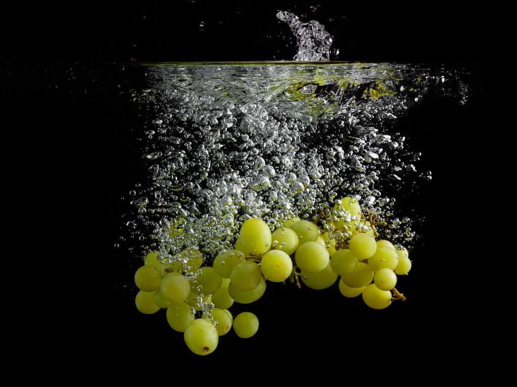 Ягоды белого винограда в воде на черном фоне