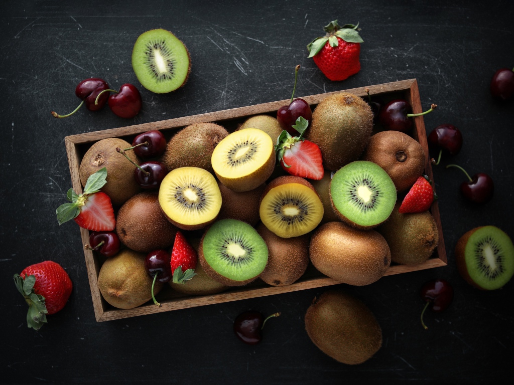 Ящик с киви, клубникой и черешней на столе 