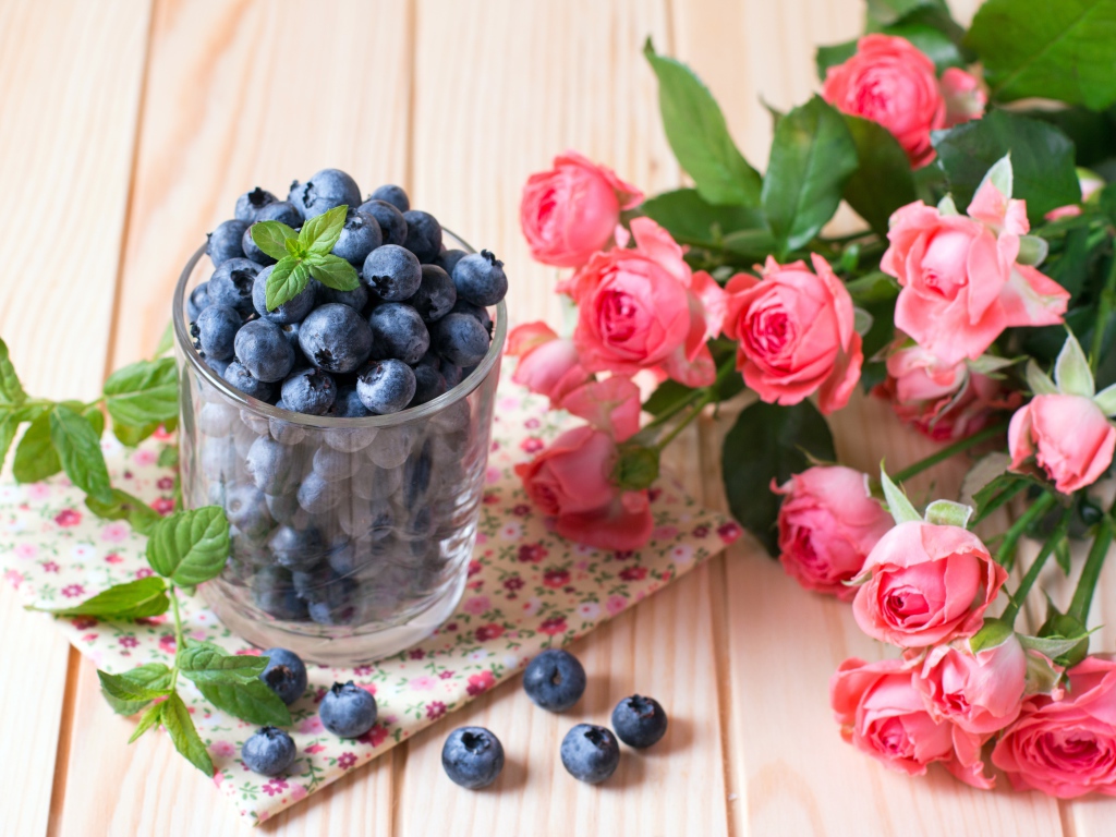 Стакан черники на столе с букетом розовых роз 
