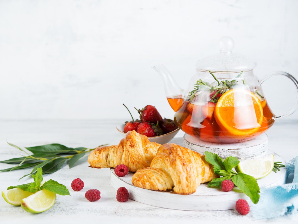Чайник с лимоном и клубникой на столе с круассанами 