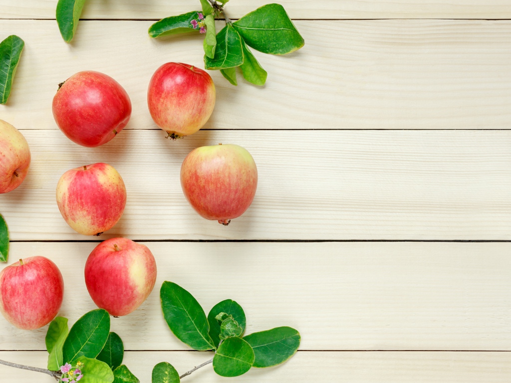 Красные яблоки с зелеными листьями на деревянном столе 