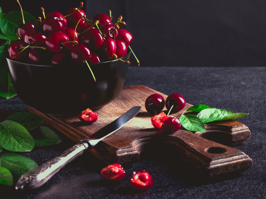 Спелые красные черешни на разделочной доске на столе 