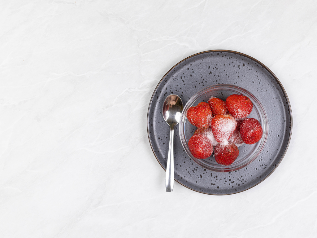 Ripe red strawberries in a bowl with sugar on a white background