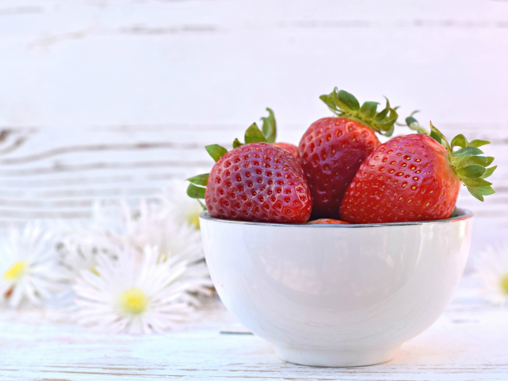Спелая клубника в белой миске на столе с ромашками