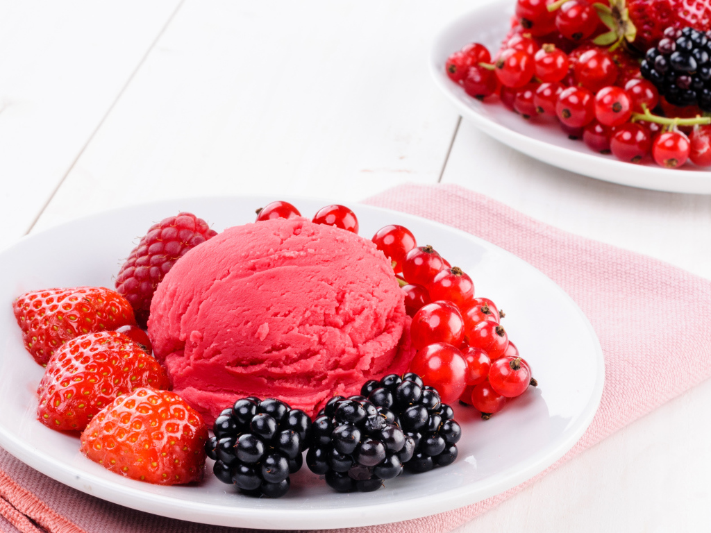 Шарик фруктового мороженого с ягодами на белой тарелке