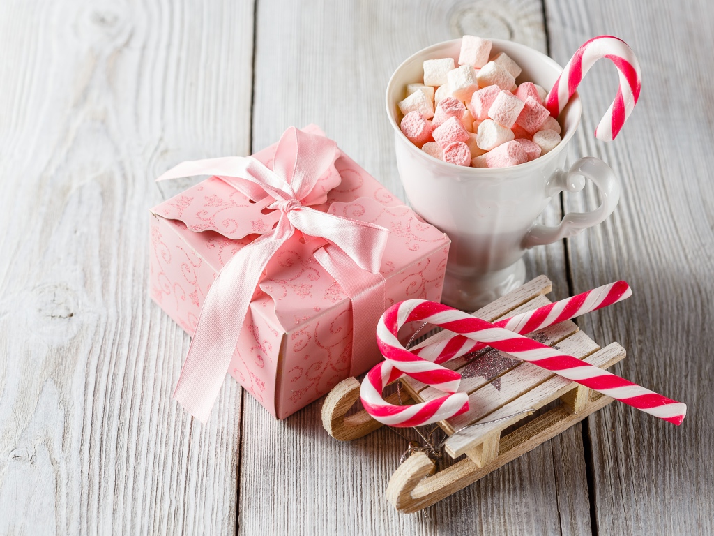 Чашка с маршмеллоу на столе с игрушечными санками и подарком