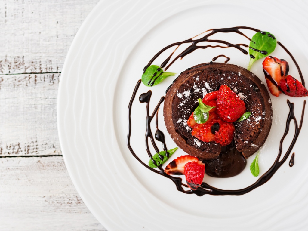 Вкусный десерт на белой тарелке с клубникой и шоколадом