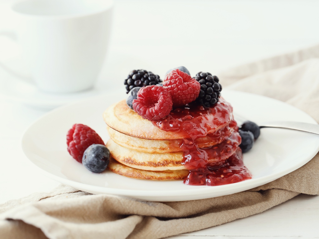 Оладьи на большой белой тарелке с джемом и ягодами 