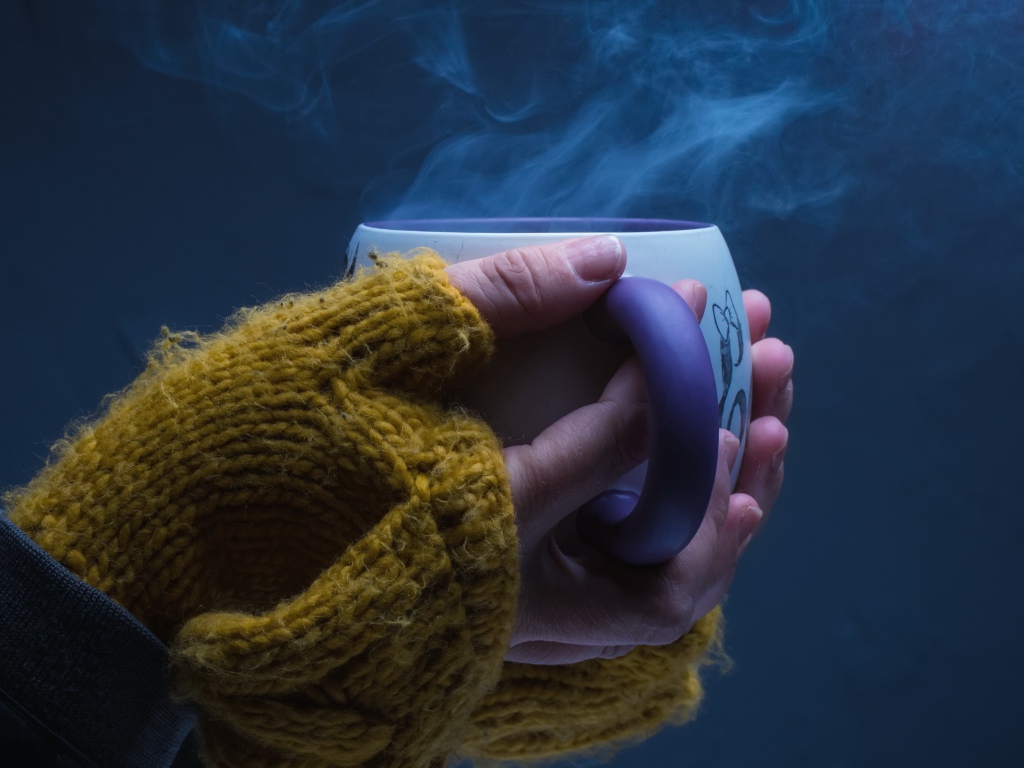 Чашка горячего кофе в руках у девушки на сером фоне