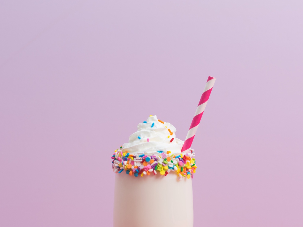 Коктейль  в стакане со взбитыми сливками на розовом фоне