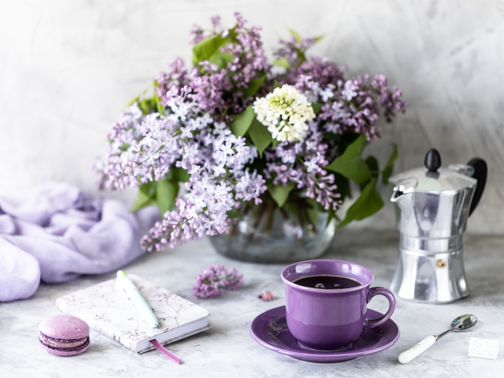 Чашка кофе на столе с блокнотом и букетом сирени в вазе