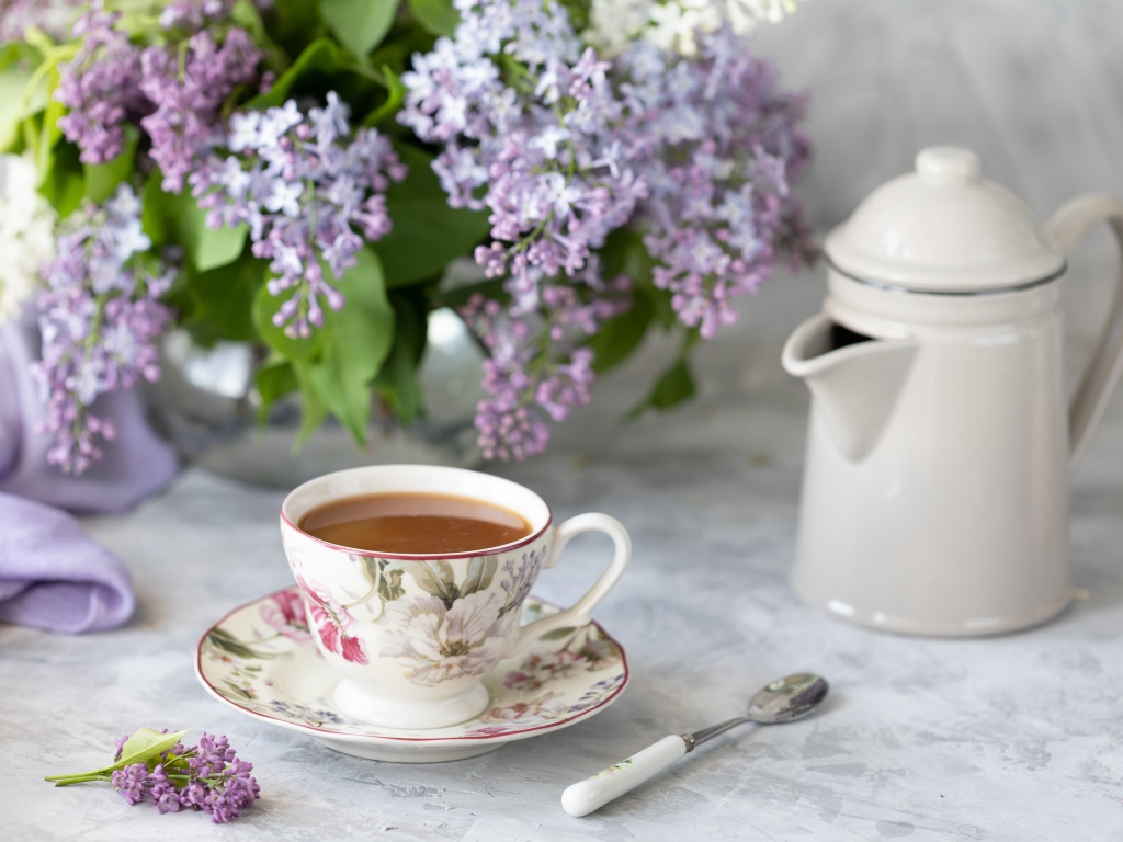 Чашка кофе с чайником на столе с букетом сирени 