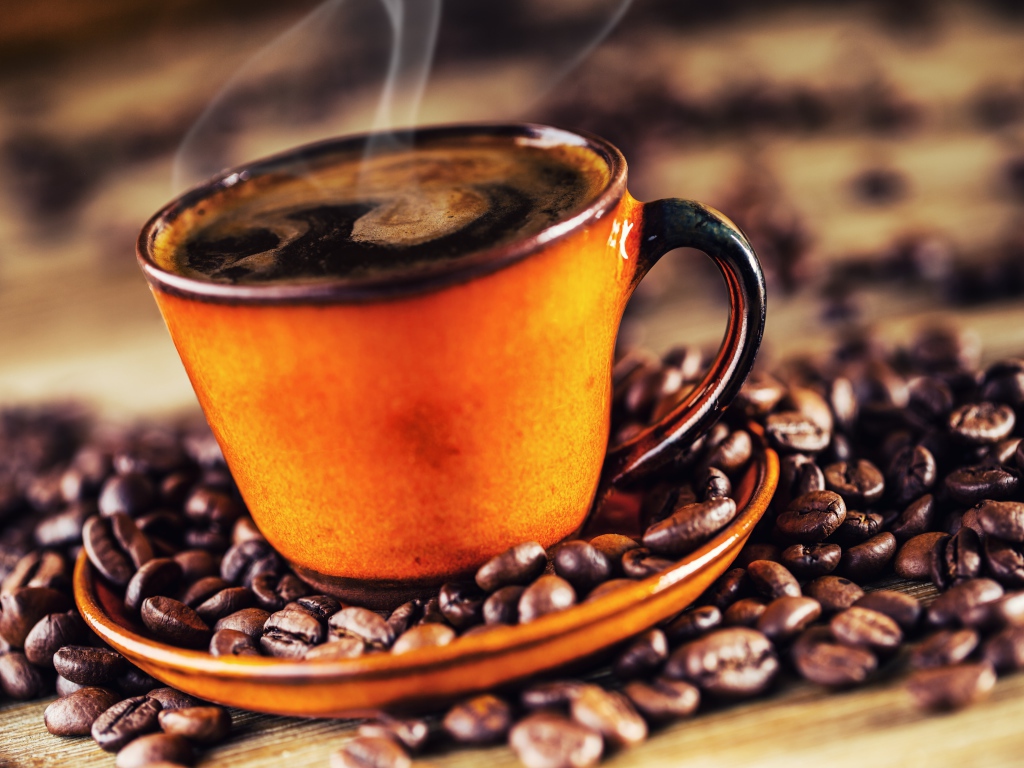 Оранжевая чашка горячего ароматного кофе на столе с зернами