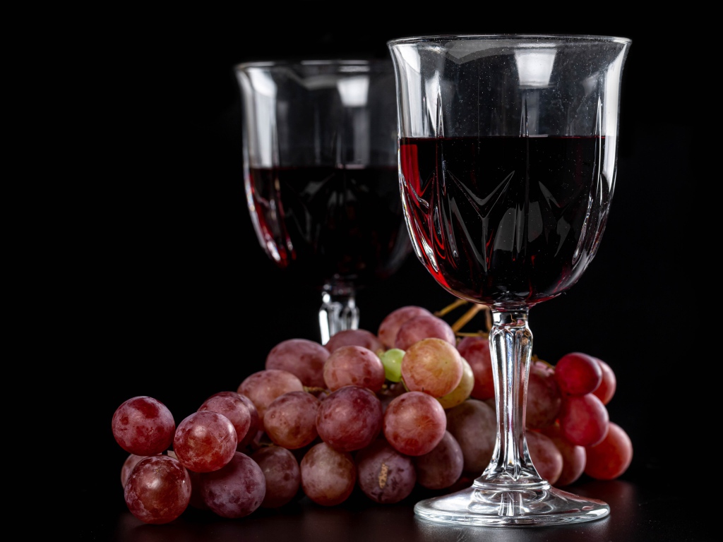 Два бокала вина на черном фоне с виноградом 