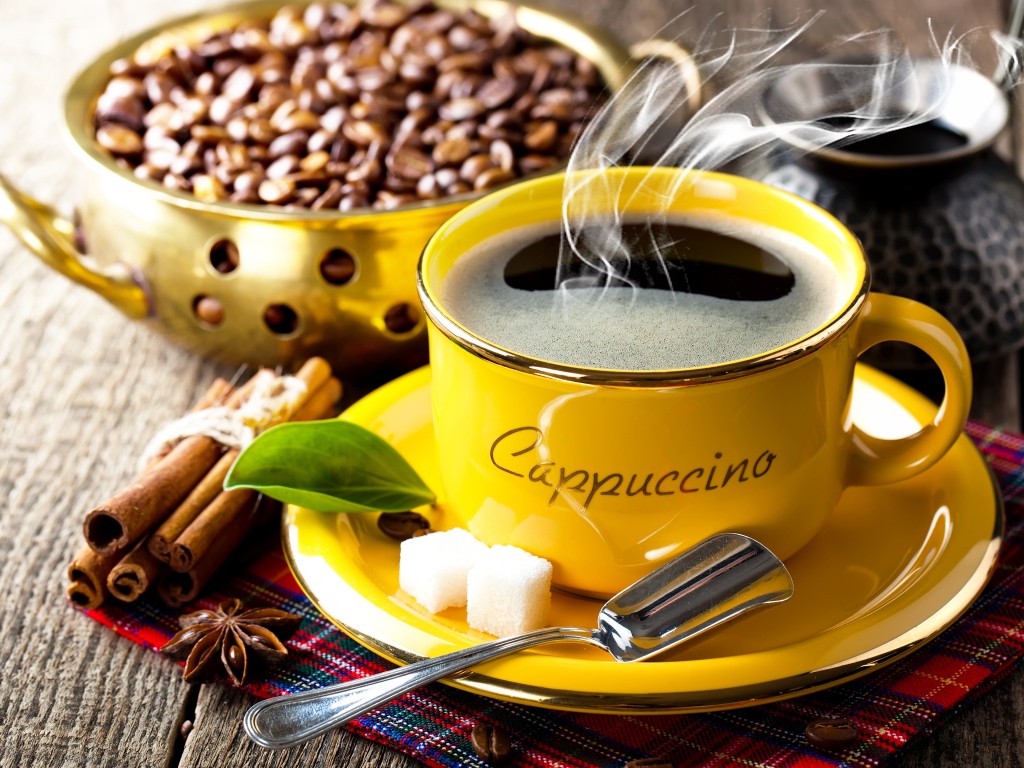 Желтая чашка с горячим кофе на столе с зернами и корицей 