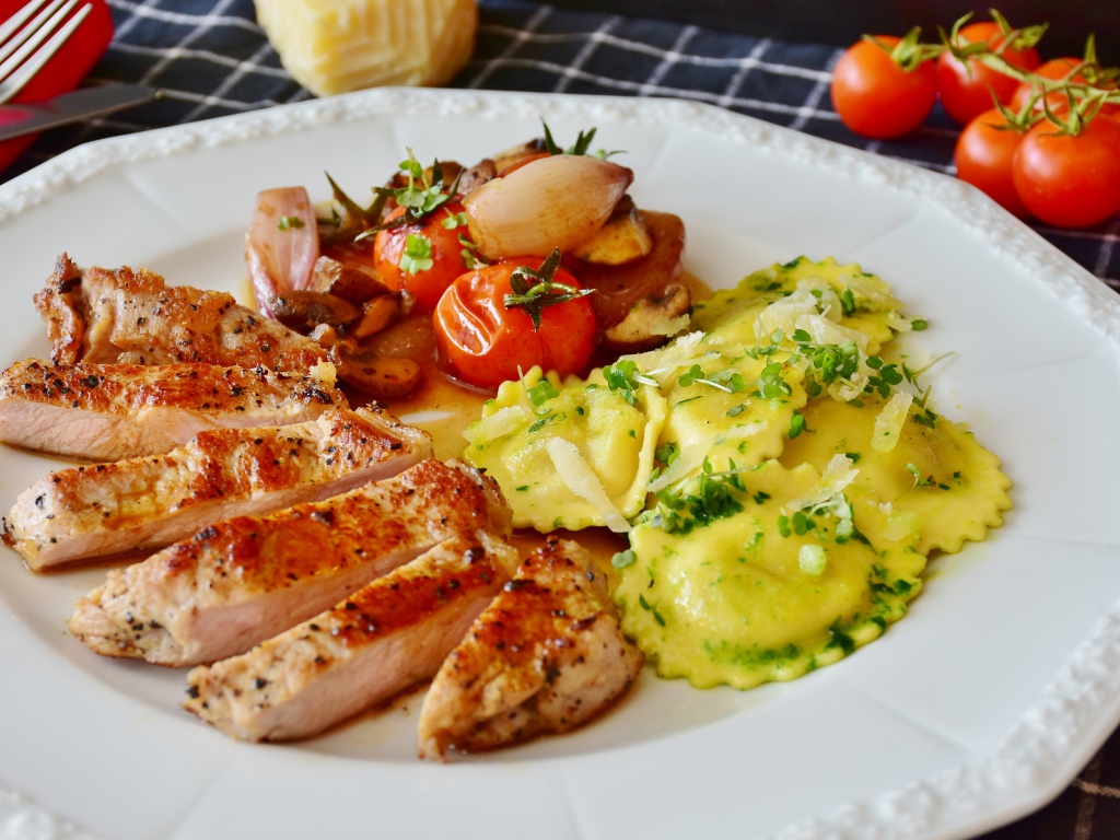 Куриное филе нарезанное кусочками на тарелке с овощами и варениками