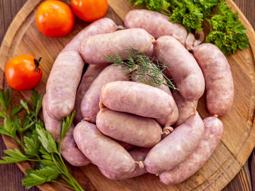 Свежие сырые домашние сардельки на доске с петрушкой и помидорами