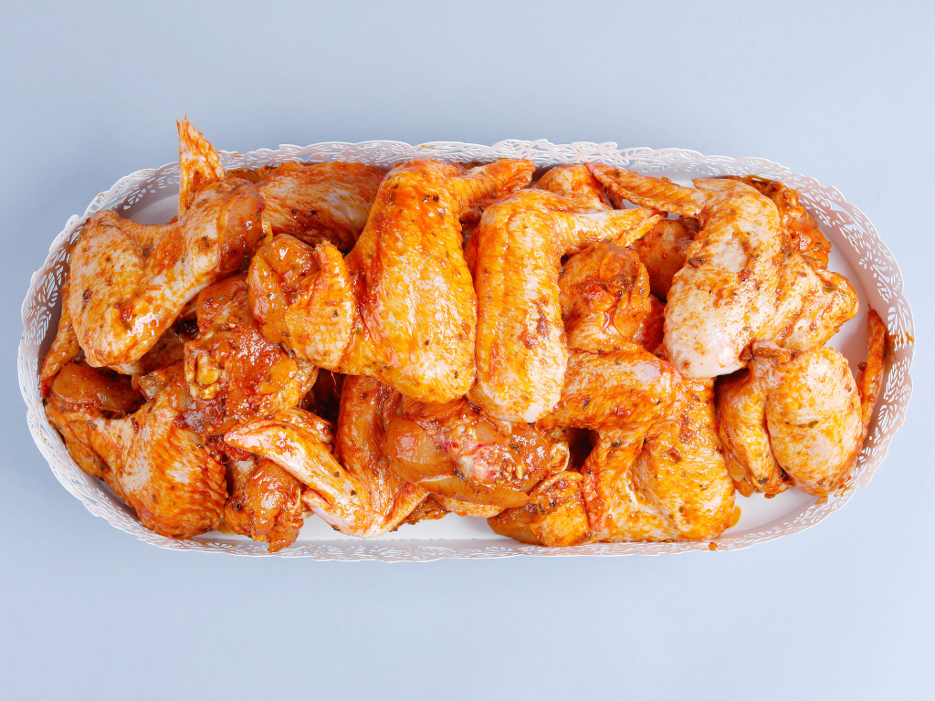 Жареные куриные крылья в белой корзине на сером фоне