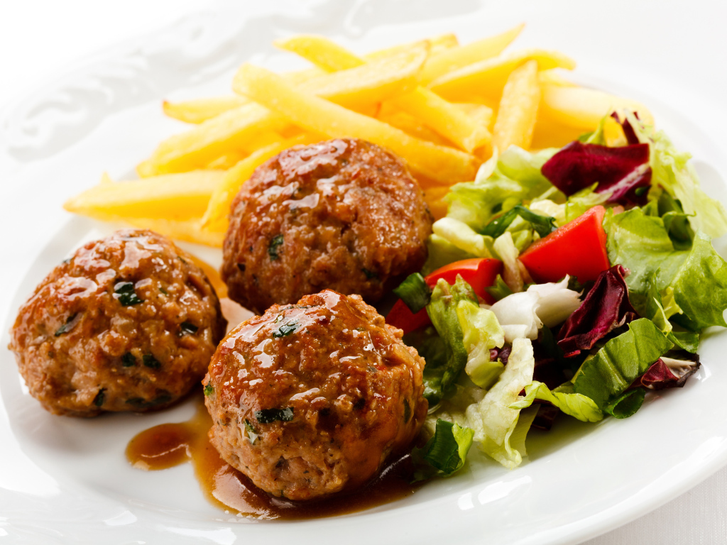 Фрикадельки с салатом и картофелем фри на белой тарелке