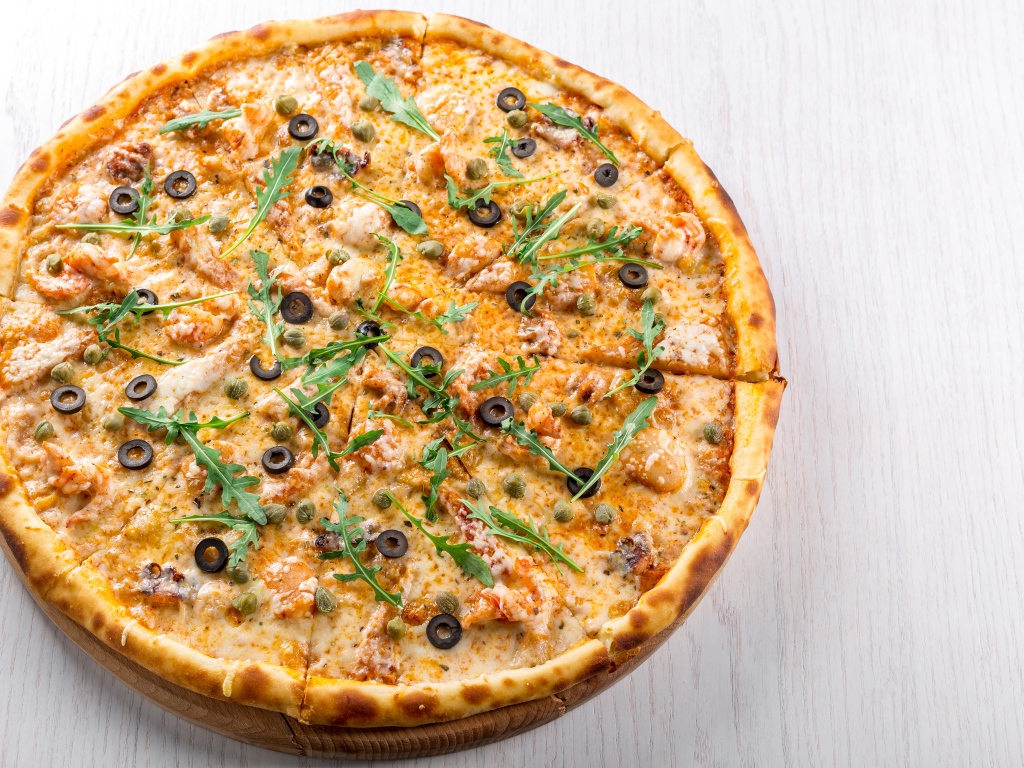 Пицца с морепродуктами, рукколой и оливками на столе 