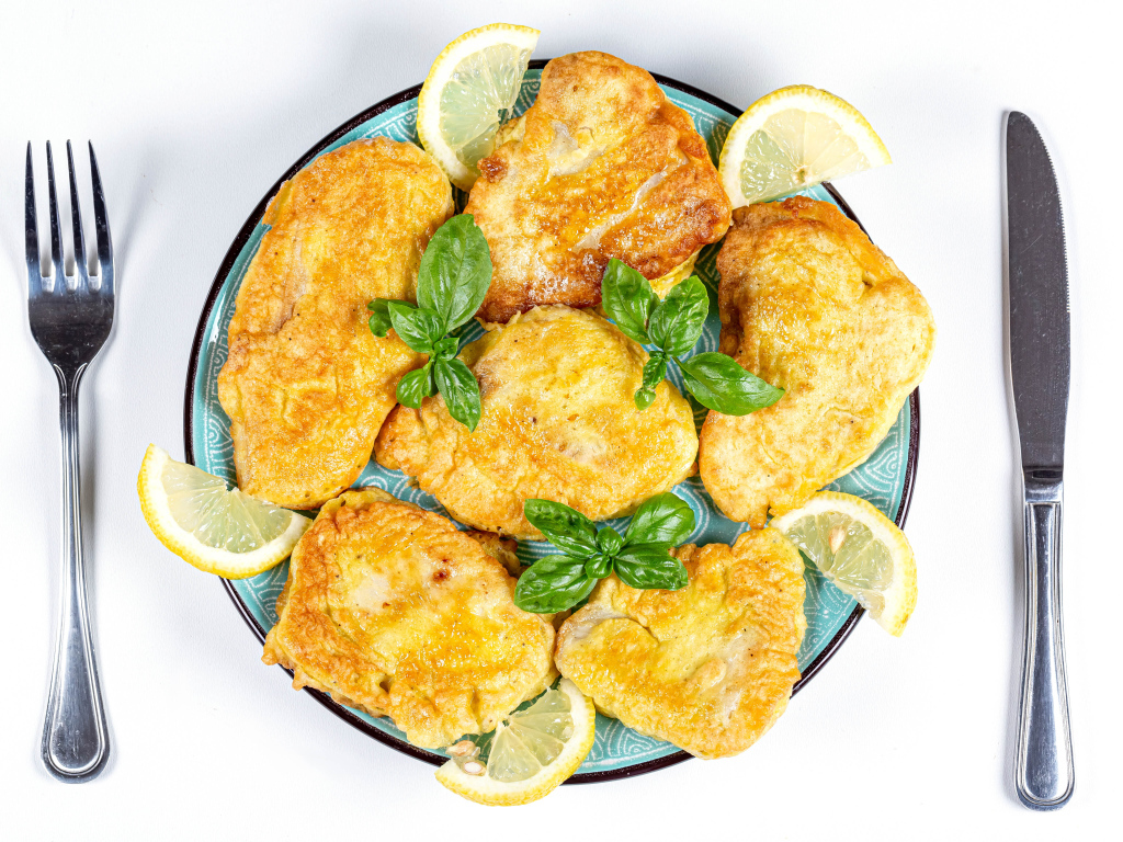 Appetizing fish in batter on a plate with lemon slices and cutlery