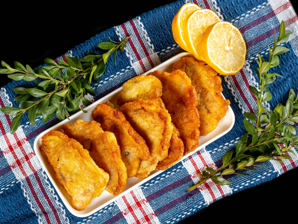 Fried fish in batter on a table with lemon and herbs