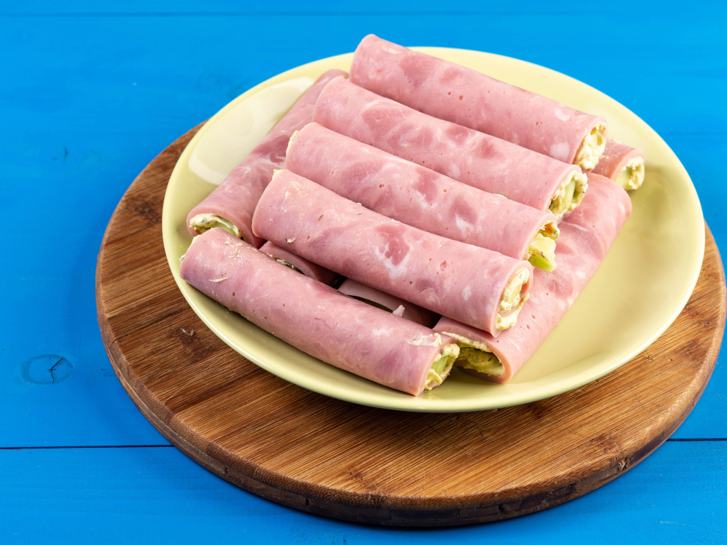 Рулетики из ветчины на тарелке на голубом столе