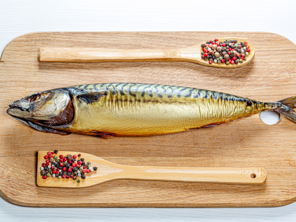 Копченая скумбрия на разделочной доске с перцем на белом фоне