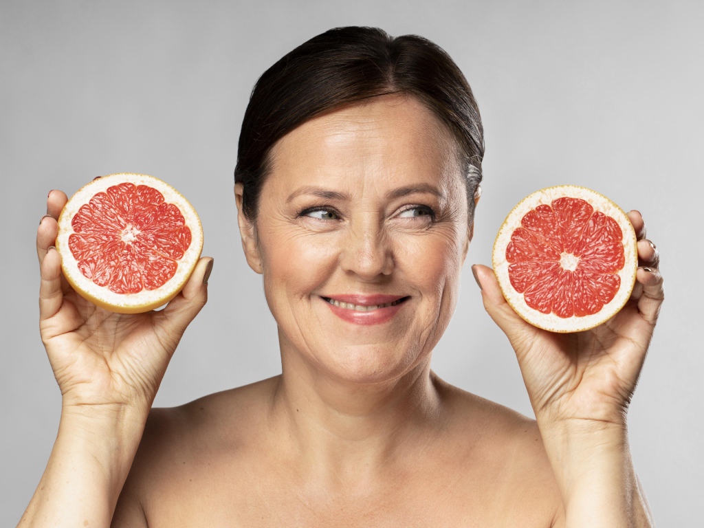 Улыбающаяся женщина с грепфрутом в руках на сером фоне