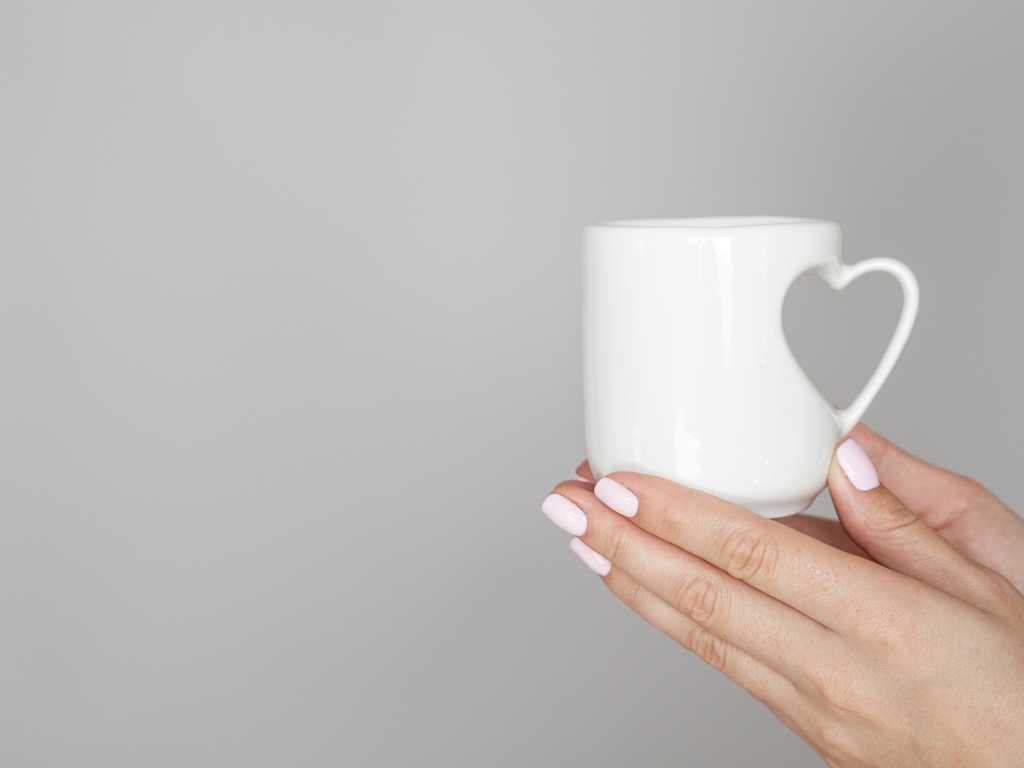 Белая кружка в руках девушки на сером фоне