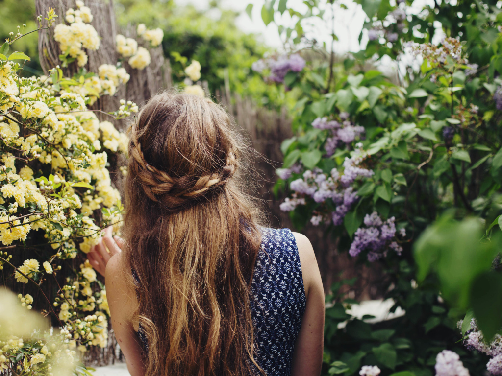 Красивая девушка с косой на голове идет по зарослям сирени 