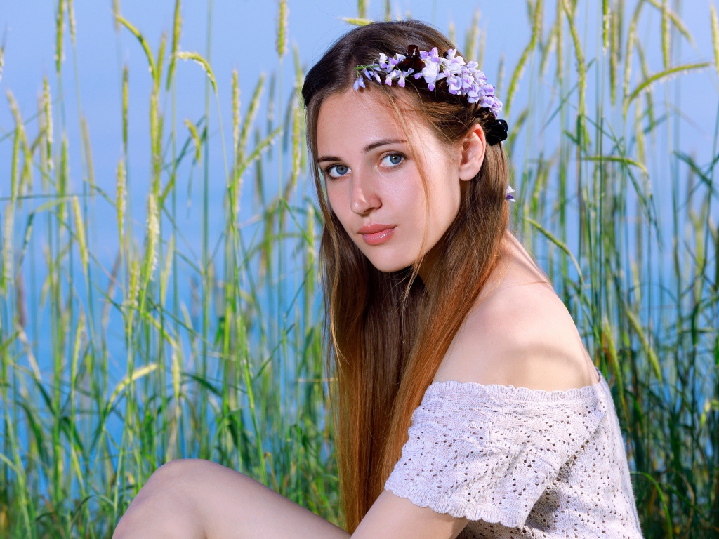 Красивая молодая девушка с венком на голове сидит на поле с колосьями 