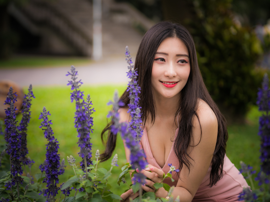 Улыбающаяся азиатка стоит у синих цветов 