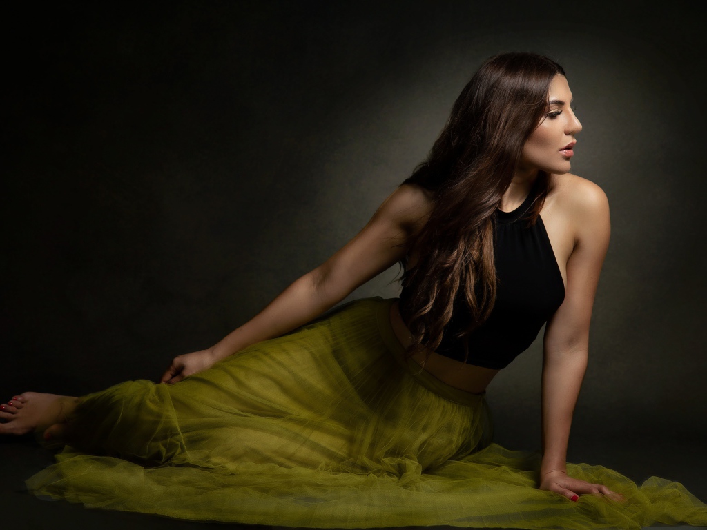 Молодая девушка в длинной юбке сидит на полу