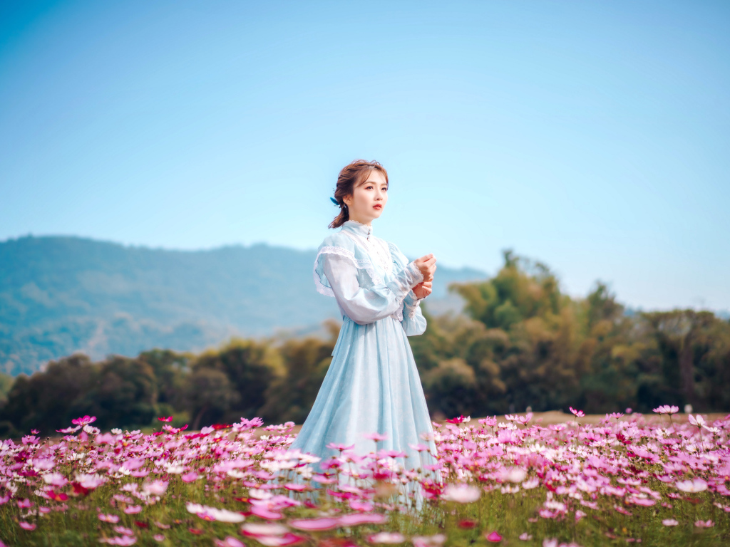 Девушка азиатка в красивом платье идет по полю с цветами космеи