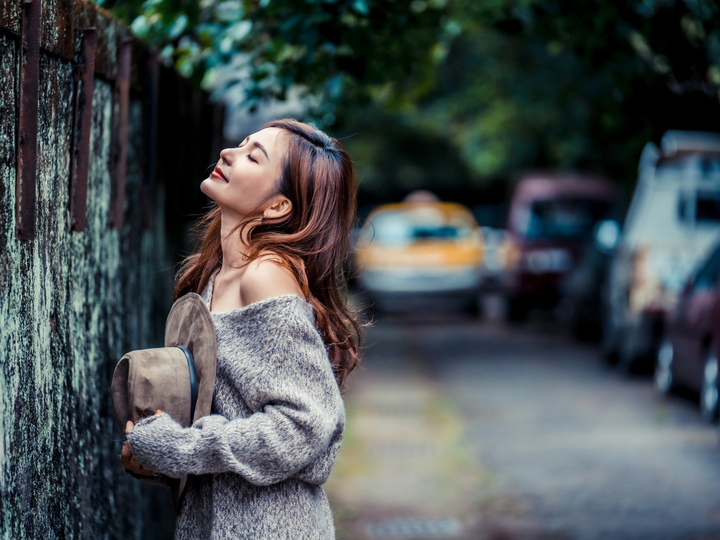 Девушка азиатка в теплом свитере стоит у забора