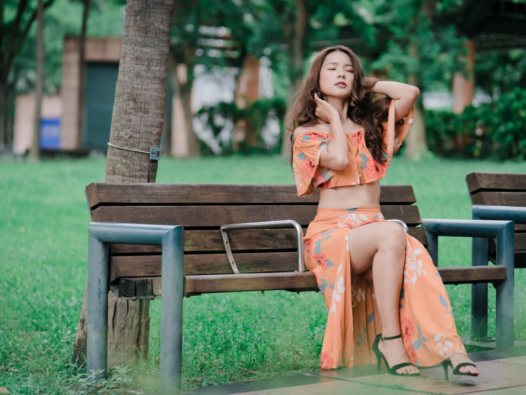 Красивая девушка азиатка в костюме сидит на лавке