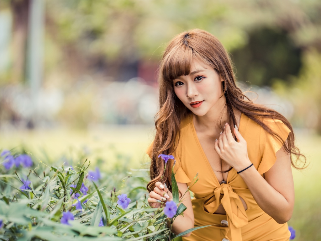 Красивая девушка азиатка в желтом платье у фиолетовых цветов 