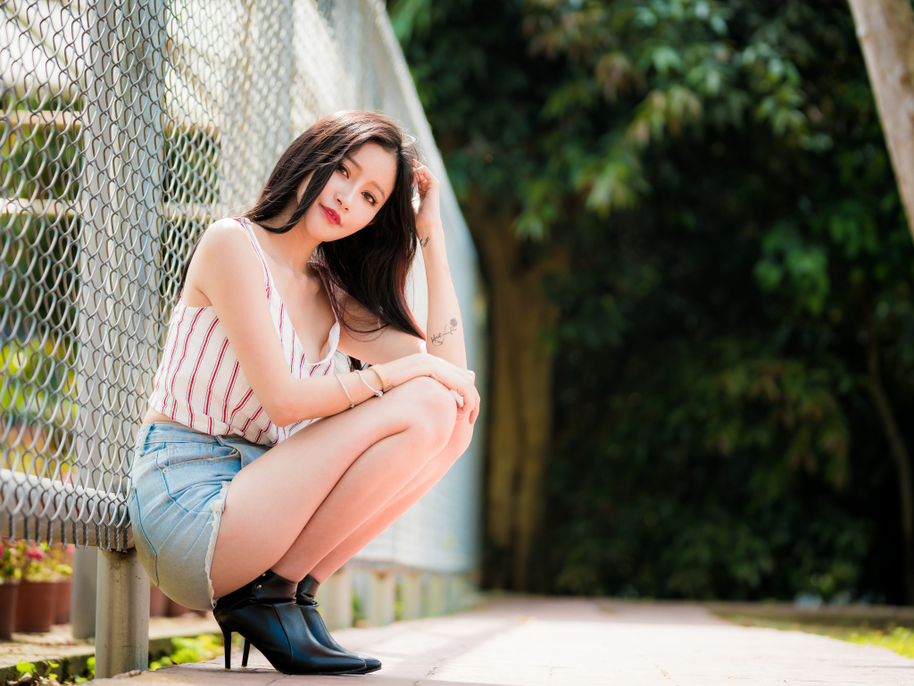 Красивая девушка азиатка сидит у железной сетки