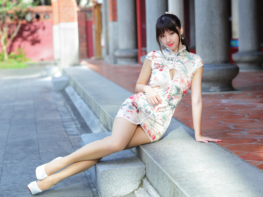 Красивая девушка азиатка в платье сидит на ступеньках