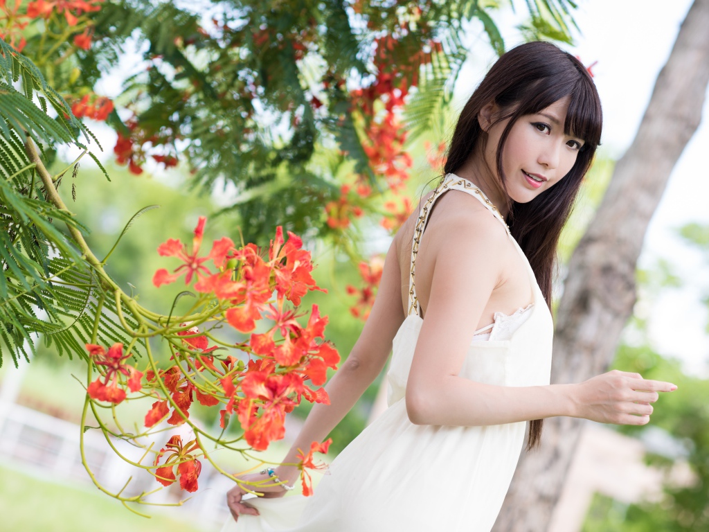 Красивая девушка азиатка в красном платье у дерева с цветами