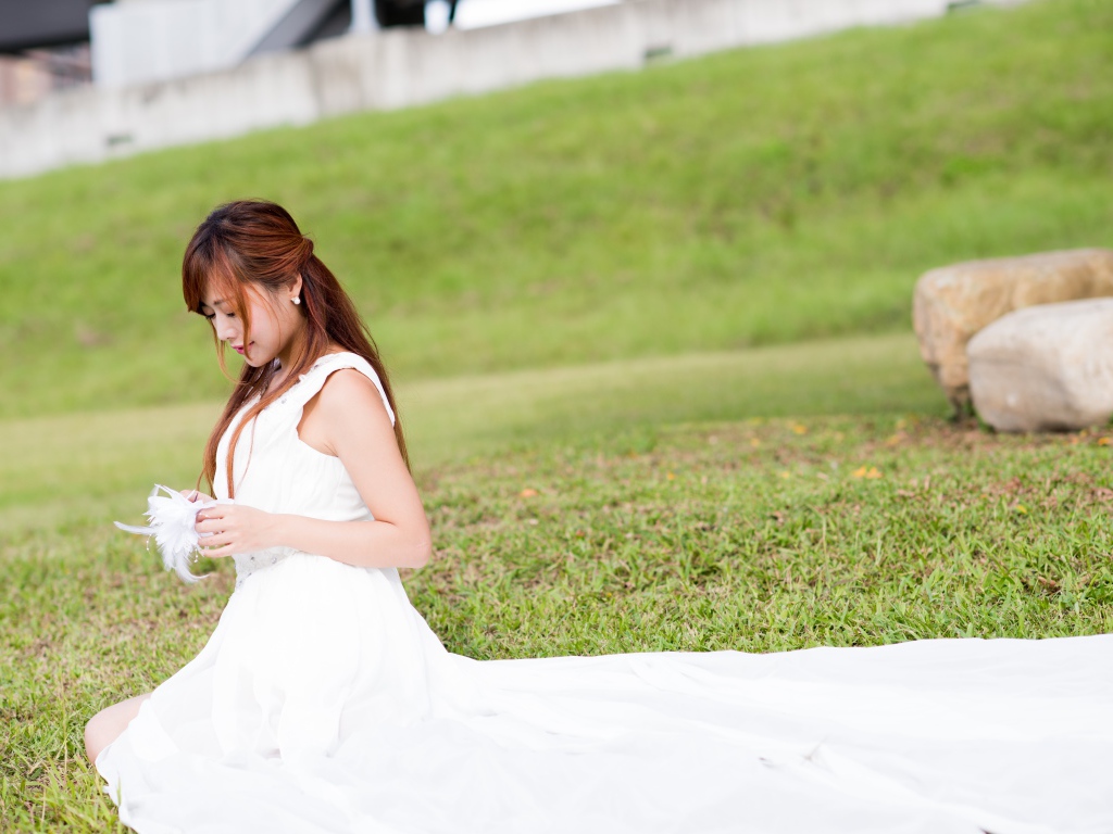 Красивая девушка азиатка в свадебном платье сидит на траве
