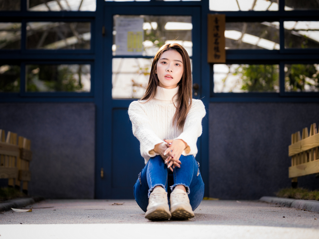 Красивая азиатка в синих джинсах сидит на земле