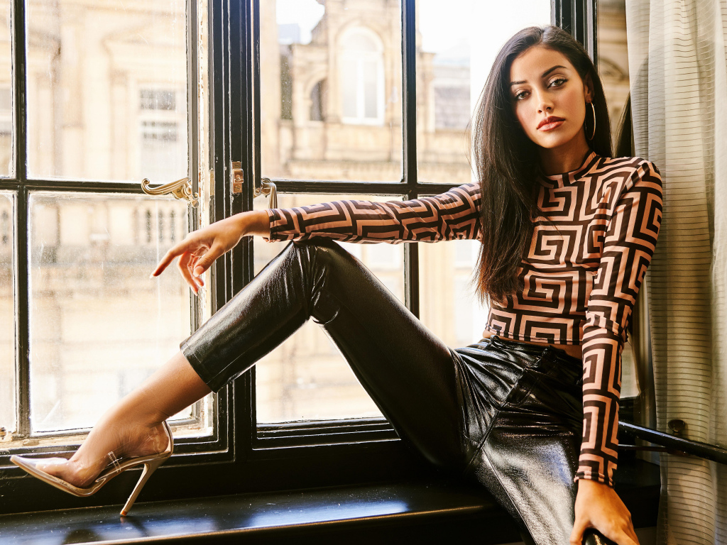 Красивая брюнетка в черных брюках сидит на окне 